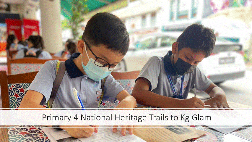 Two masked schoolboys in gray uniforms write at an outdoor table during a Primary 4 heritage trail at Kg Glam.
